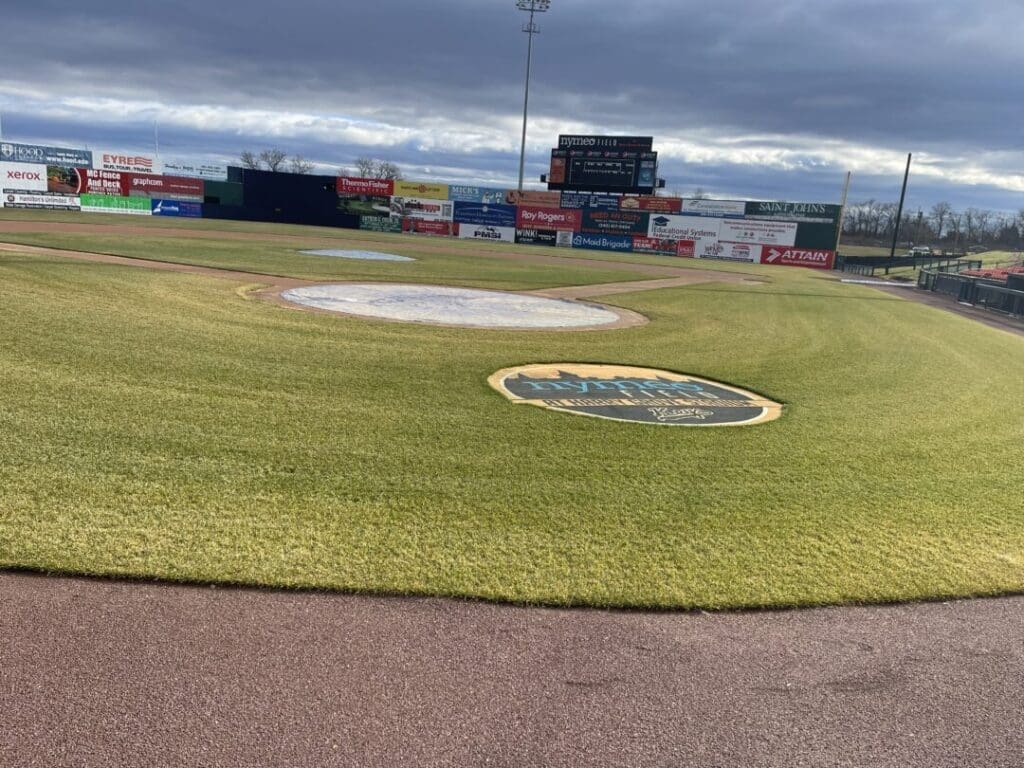 a Baseball Field with Bright Green Grass a Covered Pitching Mound and Home Plate Outfield Signs Are Visible Beyond the Scoreboard the Thunder Team Logo is Painted Near Home Plate the Cloudy Sky Looms Above As the Stadium Awaits Fans Checking the Frederick Keys Schedule