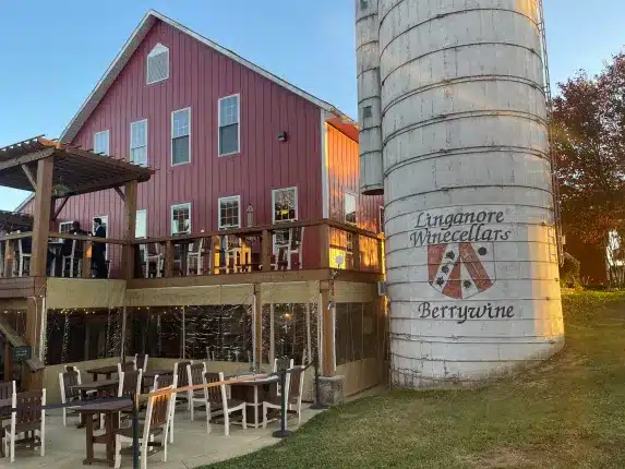 a Large Red Barn with a Wooden Deck and Outdoor Seating Stands Beside a Tall White Silo Labeled Linganore Winecellars Berrywine in New Market Md the Sunny Scene and Clear Sky Evoke a Peaceful Rural Vineyard Setting