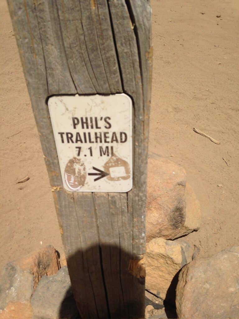 a Weathered Wooden Post Stands in Sandy Soil with Rocks at Its Base Attached is a Faded Sign Reading Phils Trailhead 71 Mi with Black Text and a Right Pointing Arrow Marking One of the Top Things to Do in Bend or for Outdoor Lovers