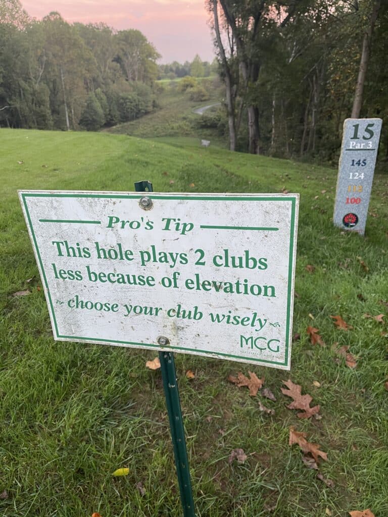 a Golf Course Tee in Mt Airy Md Features a Sign This Hole Plays 2 Clubs Less Because of Elevationchoose Your Club Wisely to the Right a Stone Marker Notes Hole 15 Par 3 with Distances Listed Trees and Fairway Stretch into the Background