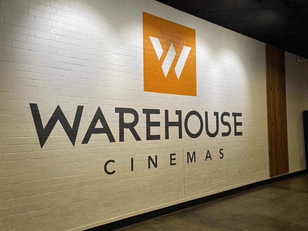 a Large White Brick Wall Features the Bold Black Words Warehouse Cinemas and an Orange Square Above with a White Stylized W Logo the Polished Concrete Floor and Wood Paneling Create a Modern Vibeone of the Top Things to Do in Frederick Md