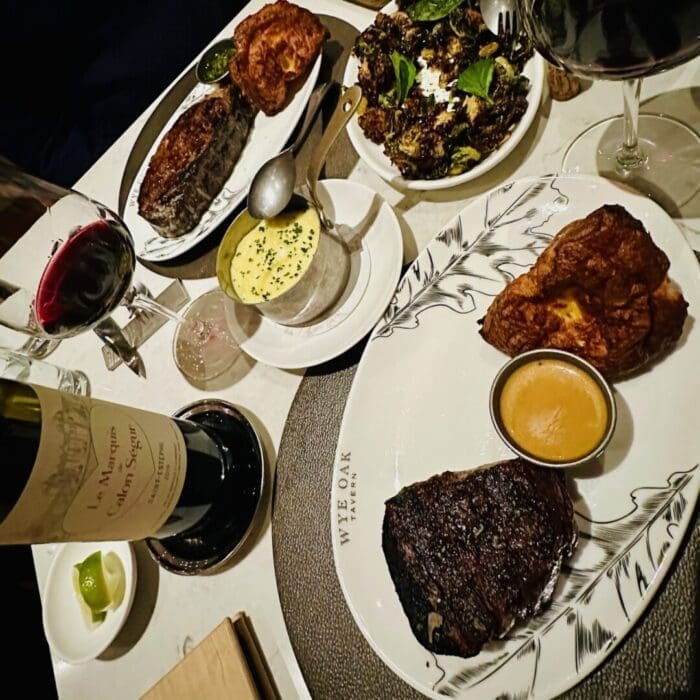 a Restaurant Table Set with Plates of Grilled Steak Yorkshire Pudding Roasted Broccoli Sauce and a Glass of Red Wine at Wye Oakthe Best Steakhouse Frederick Md Has to Offerwhere the Food is Artistically Arranged on Elegant White Dishes