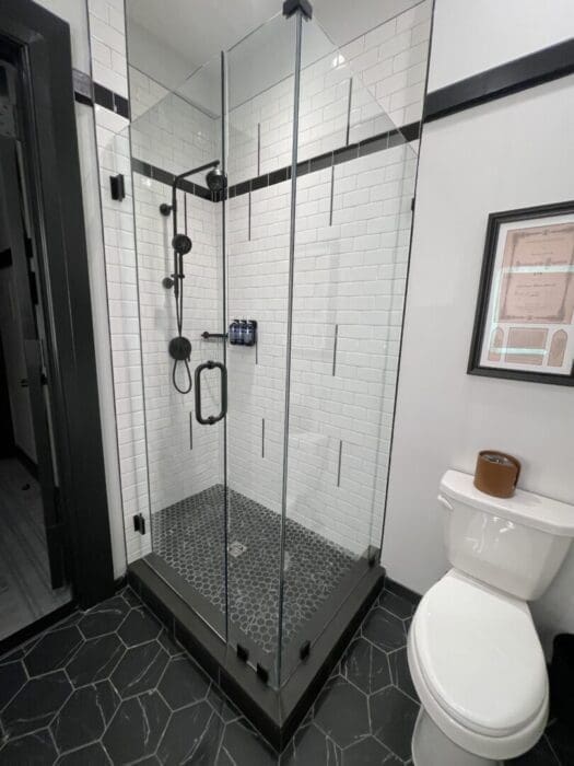 Visitation hotel frederick room bathroom a Modern Bathroom at Visitation Hotel Frederick Md Features a Glass Shower with White Subway Tile Walls Black Fixtures and Hexagonal Black Tile Floor Outside the Shower is a White Toilet Black and White Walls a Framed Picture and Sleek Finishes Throughout