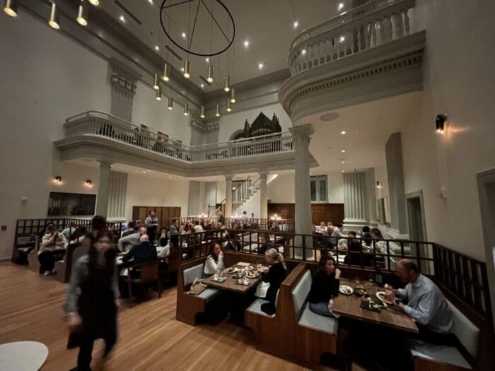 a Spacious Elegant Restaurant with High Ceilings Chandeliers and a Balconyperfect for Guests from Boutique Hotels Frederick Md Soft Lighting Wooden Floors and Classical Details Create a Warm Atmosphere As Diners Enjoy Meals and Attentive Service