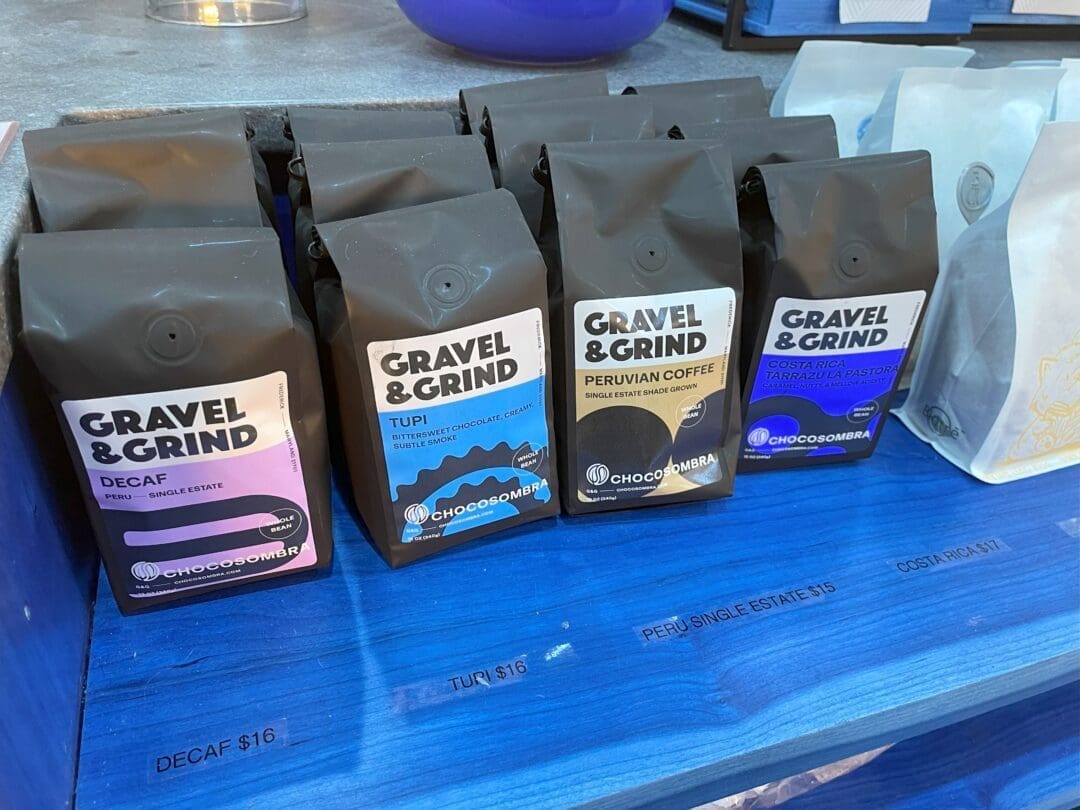 Gravel and grind coffee Four Black Bags of Gravel Grind Coffee Are Displayed on a Bright Blue Shelf in a Coffee Shop Frederick Md Each Bag is Labeled Decaf Tupi Peruvian Coffee and Coopedota Rl Partial Prices and More Coffee Bags Are Visible on Either Side