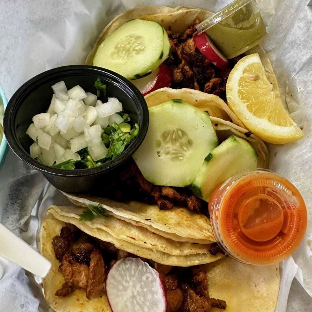 Three Street Tacos Filled with Grilled Meat Sliced Radish and Cucumber Are Served on Soft Corn Tortillas Enjoy Them on a Tray with a Lemon Wedge Salsa and Toppingsjust Like at the Spots Serving the Best Pupusas in Frederick Md