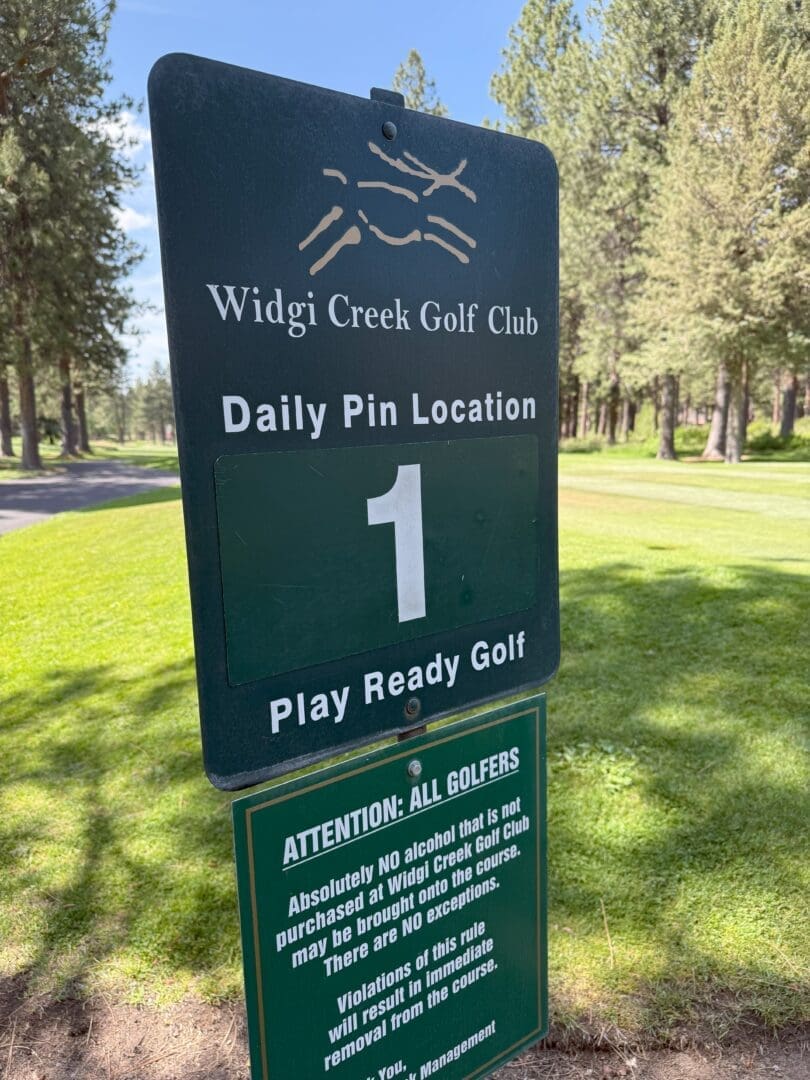a Green Sign at Widgi Creek Golf Club Displays Daily Pin Location 1 and Play Ready Golf Below a Notice Warns That Outside Alcohol is Not Allowed and Violations May Result in Removal Trees and Green Grass Are Visible in the Background