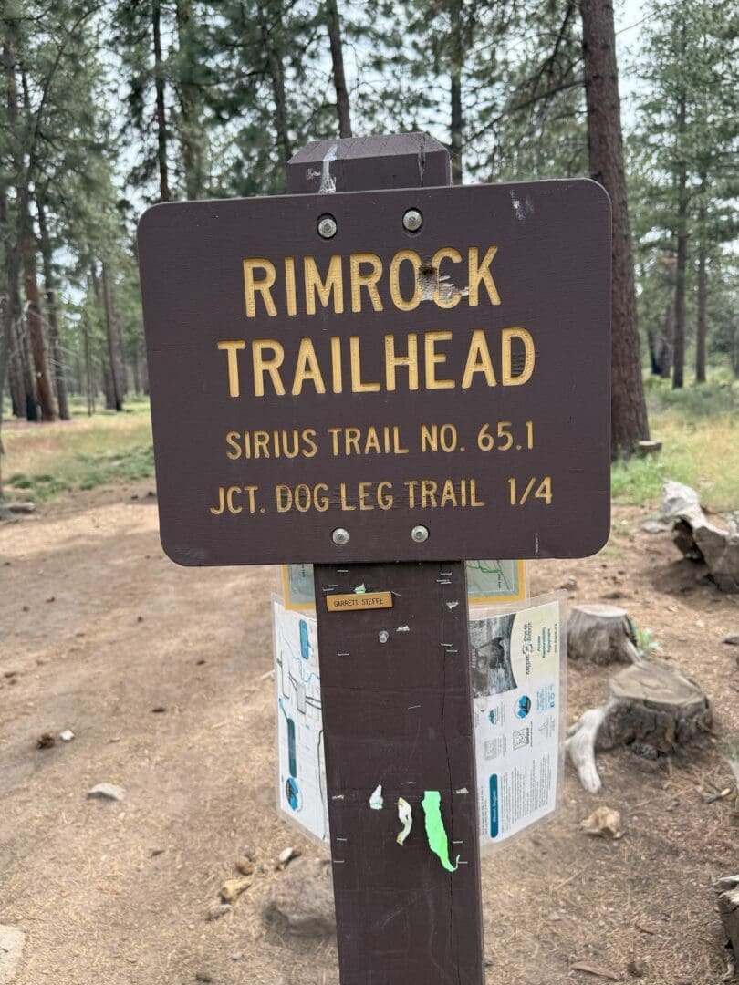 a Brown Wooden Sign Reads Rimrock Trailhead Sirius Trail No 651 Jct Dog Leg Trail 14 Surrounded by Pine Trees and a Trail Map This Scenic Spot is Perfect for Those Seeking Classic Bend Hikes or Memorable Hikes Near Bend Oregon
