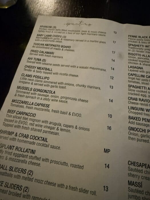 a Close up Photo of a Restaurant Menu at Cucina Massi Frederick Md on a Dark Table Showing Items Like Arancini Lamb Chops Antipasto Board Spicy Calamari Meatballs Fried Mozzarella Caprese Shrimp Cocktail Rollatini and Sliders with Prices Listed
